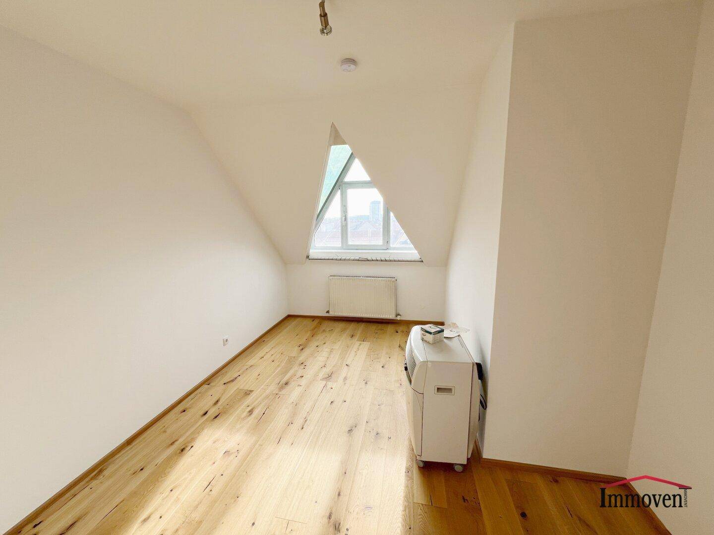 Heller Dachraum mit Holzboden und schrägen Wänden, ausgestattet mit einer Klimaanlage.