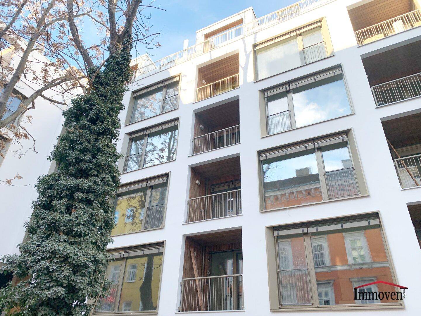 Moderne Gebäudefassade mit großen Fenstern und mehreren Balkonen in einem städtischen Umfeld.