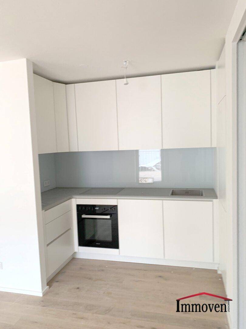 Moderne Küchenzeile mit weißen Schränken, integriertem Backofen und Induktionskochfeld.