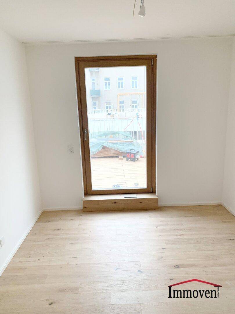Helles Schlafzimmer mit Holzboden und großem Fenster, das Zugang zu einem Außenbereich bietet.