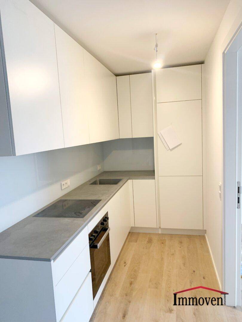 Moderne Einbauküche mit weißen Schränken, grauer Arbeitsplatte und Induktionskochfeld.