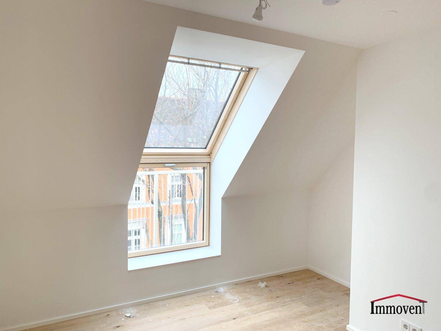 Dachgeschosszimmer mit schräger Decke und einem großen Fenster für viel Tageslicht.