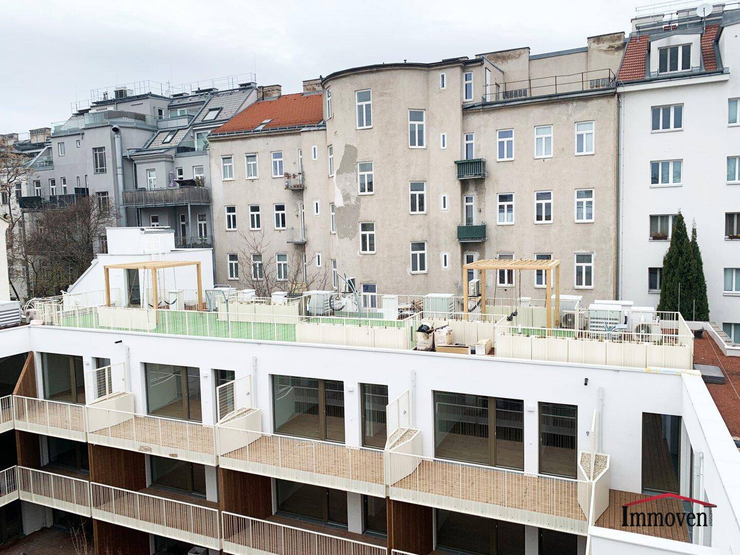 Moderne Gebäudefassade mit mehreren Balkonen und Terrassen, im Hintergrund ältere Stadtgebäude.