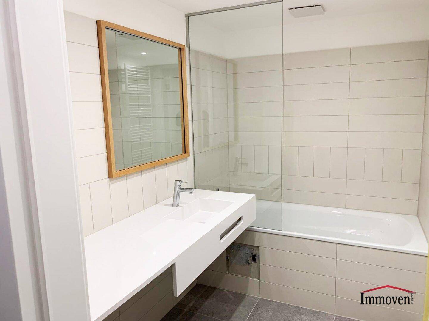 Modernes Badezimmer mit Badewanne, schwebendem Waschtisch und großen Fliesen.