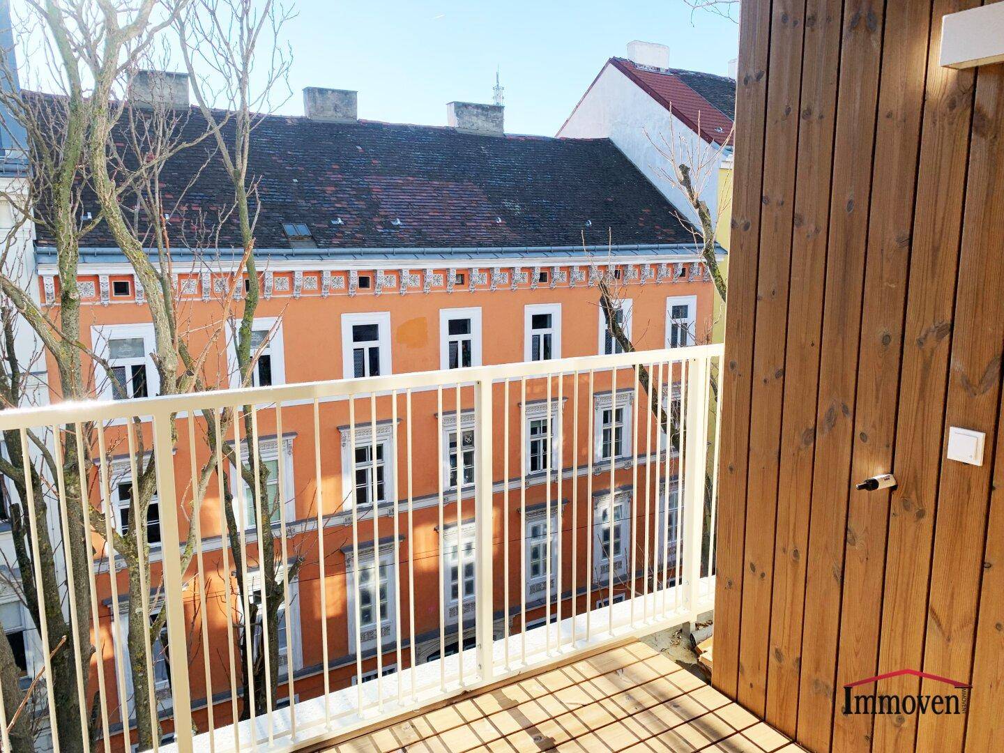 Sonniger Balkon mit Holzboden und Blick auf die gegenüberliegende Häuserzeile.