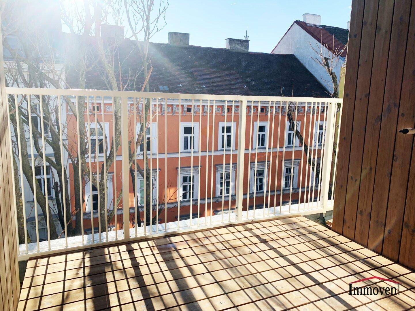 Sehr sonniger Balkon mit Holzdielen und weitem Blick über die Stadt.