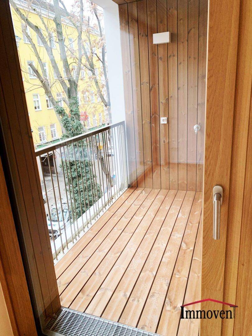 Kleiner Holzbalkon mit Metallgeländer und Blick auf die umliegenden Gebäude und Bäume.