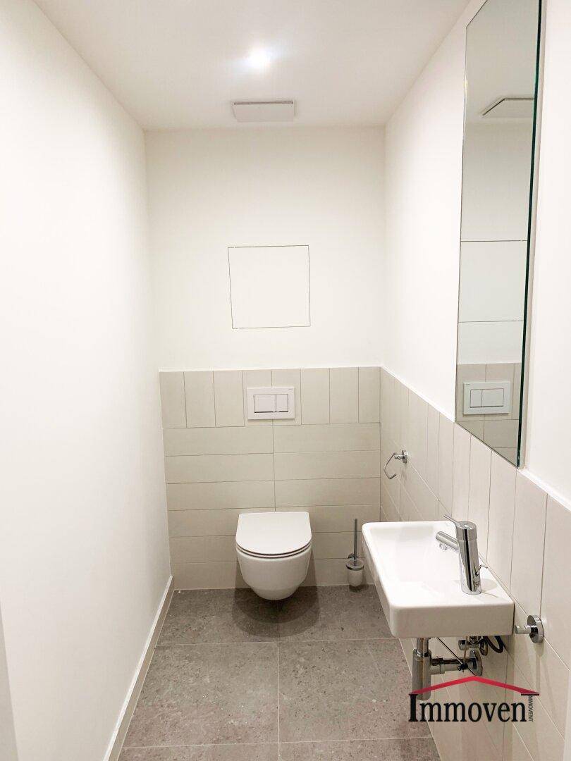 Modernes Gäste-WC mit wandhängender Toilette, kleinem Waschbecken und Fliesenboden.