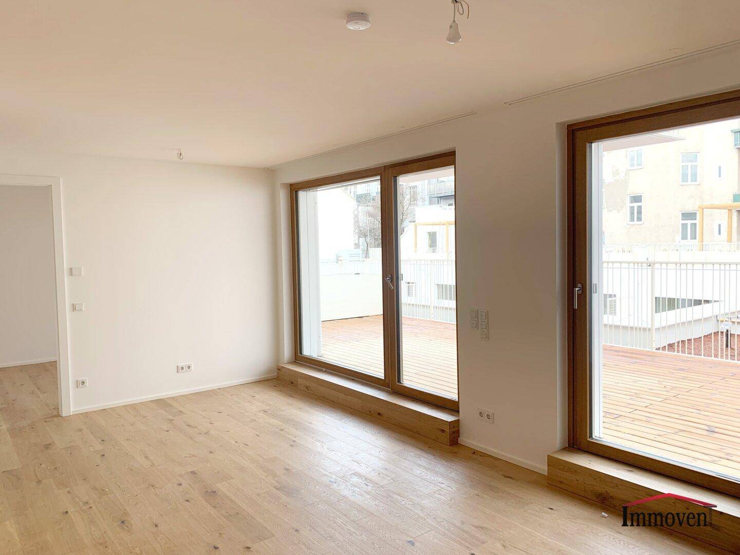 Geräumiges, helles Zimmer mit Holzboden und großen Fenstern, die viel Tageslicht hereinlassen.