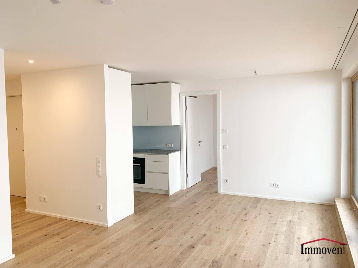 Offener Wohnbereich mit integrierter Küchenzeile und hellem Holzboden, ideal für modernes Wohnen.