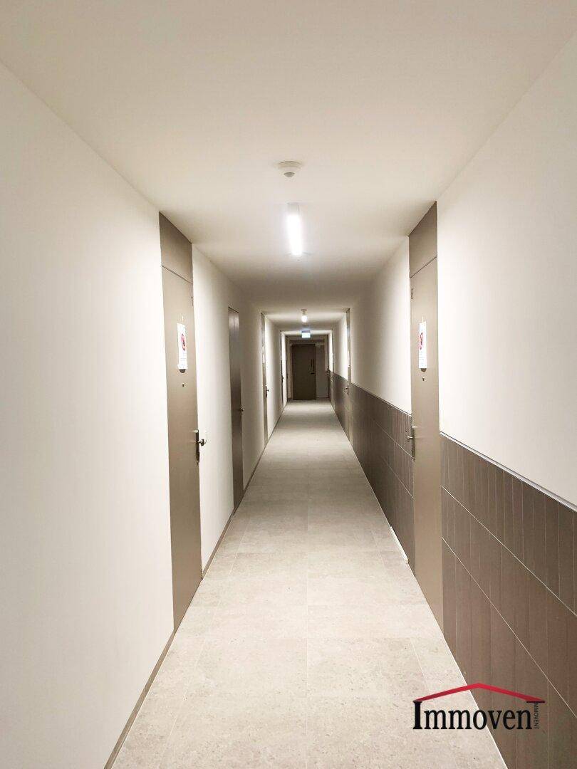 Langer, heller Flur in einem Mehrfamilienhaus mit vielen Wohnungstüren.
