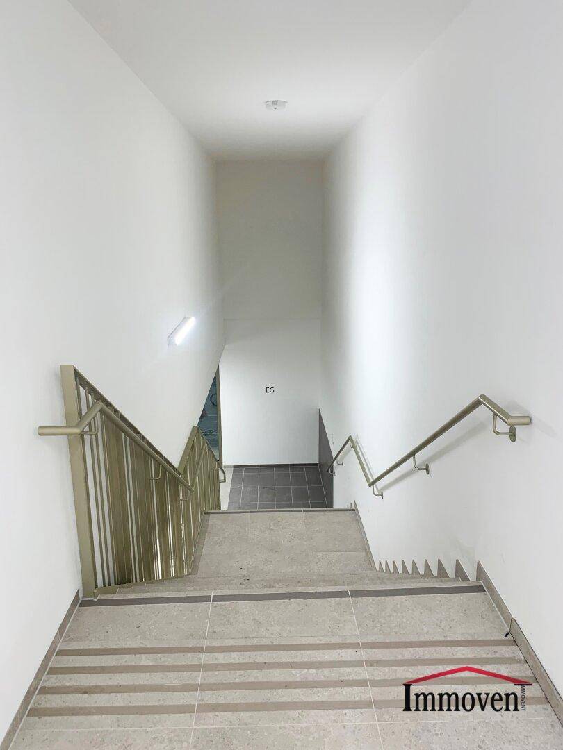 Treppenhaus mit hellem Anstrich und Metallgeländer, führt ins Erdgeschoss.