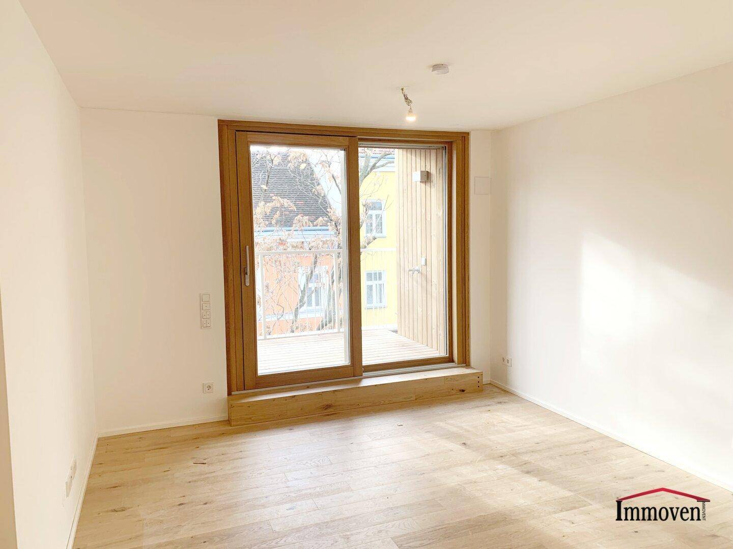 Heller, leerer Raum mit Holzboden und Zugang zu einem Balkon.