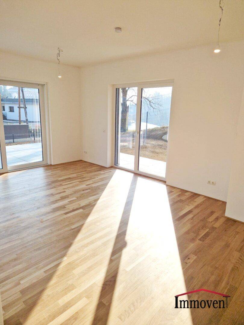 Geräumiger Wohnraum mit Parkettboden und großen Fenstern, die viel Tageslicht hereinlassen.