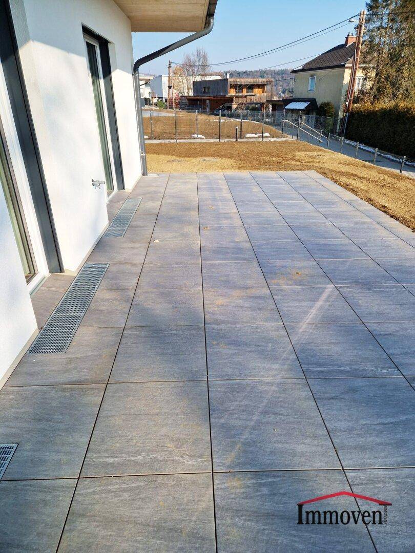Geräumige, geflieste Terrasse mit Entwässerungsrinnen und Blick auf die Umgebung.