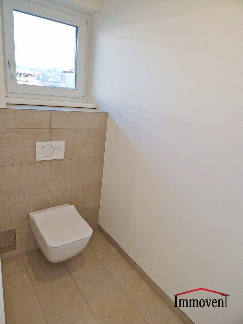 Separates WC mit wandhängender Toilette und kleinem Fenster für Belüftung.