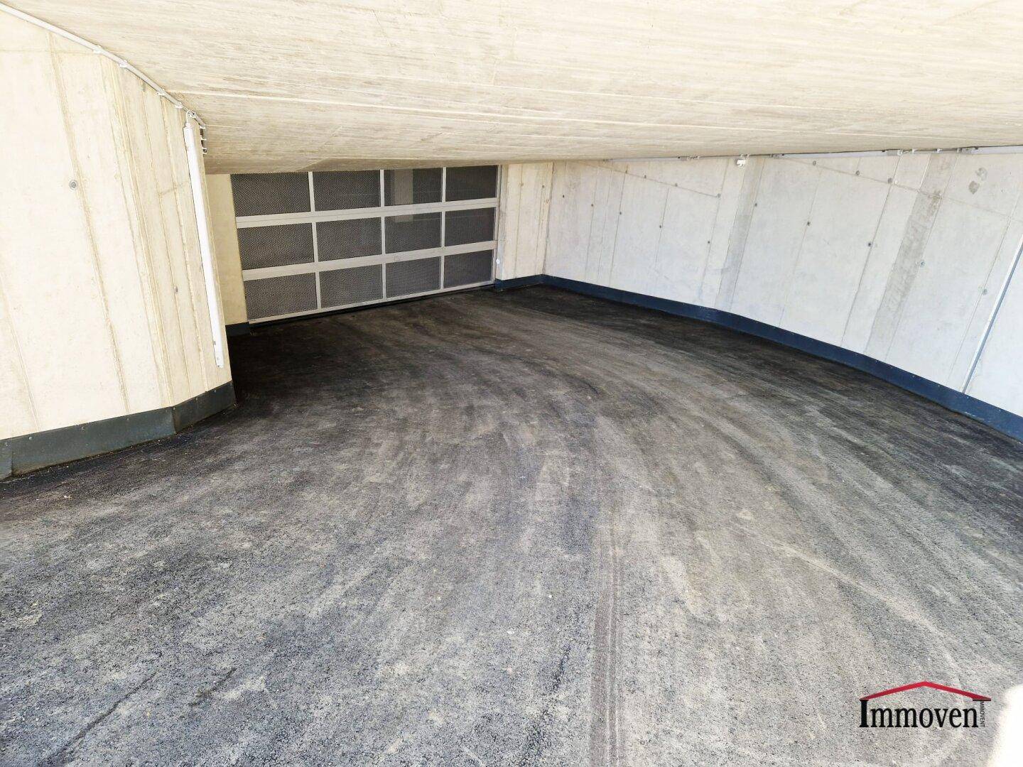 Zufahrt zur Tiefgarage mit asphaltiertem Boden und Betonwänden.