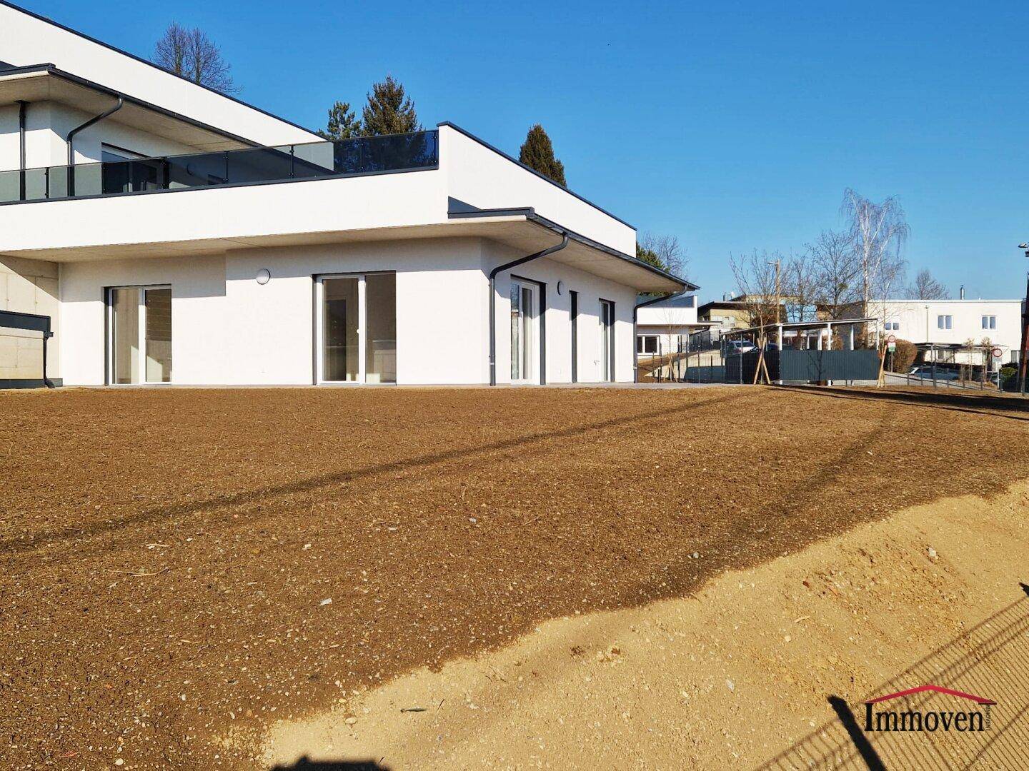 Neu angelegter Gartenbereich mit vorbereitetem Boden für Bepflanzung und moderner Architektur im Hintergrund.