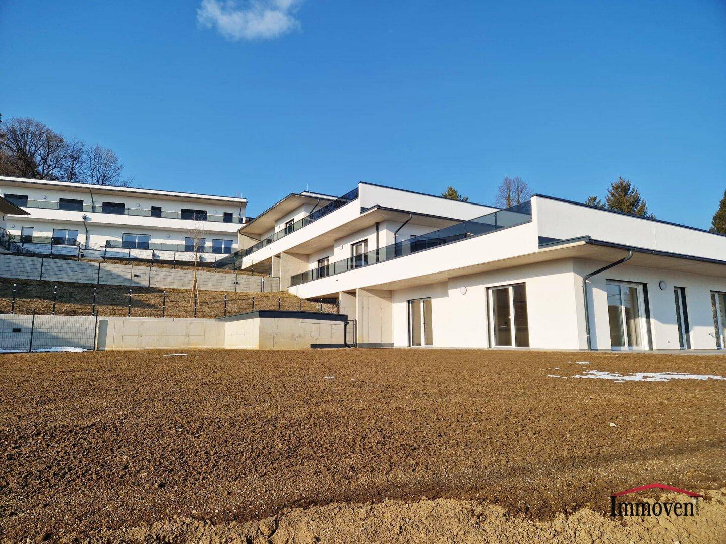 Weitläufiger Gartenbereich mit Blick auf mehrere moderne Neubaugebäude unter blauem Himmel.
