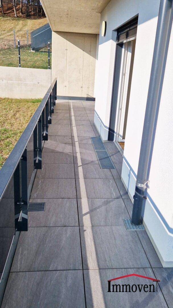 Lange, geflieste Terrasse mit modernem Geländer und Entwässerungsrinnen.