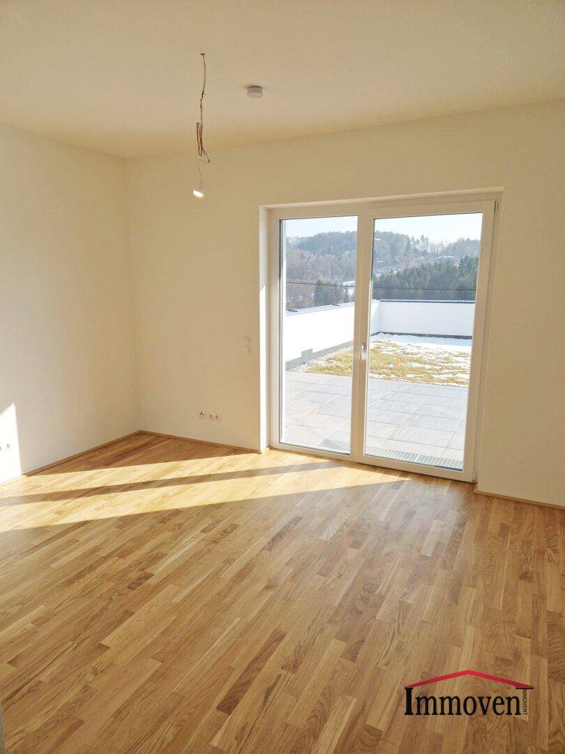 Geräumiges Zimmer mit Holzboden und großen Fenstern, die viel Sonnenlicht hereinlassen.
