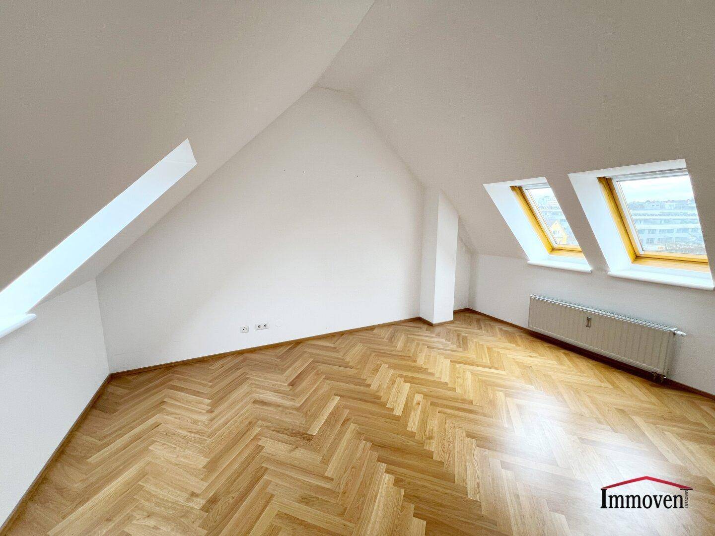 Helles Schlafzimmer im Dachgeschoss mit Parkettboden, schrägen Wänden und zwei Dachfenstern.