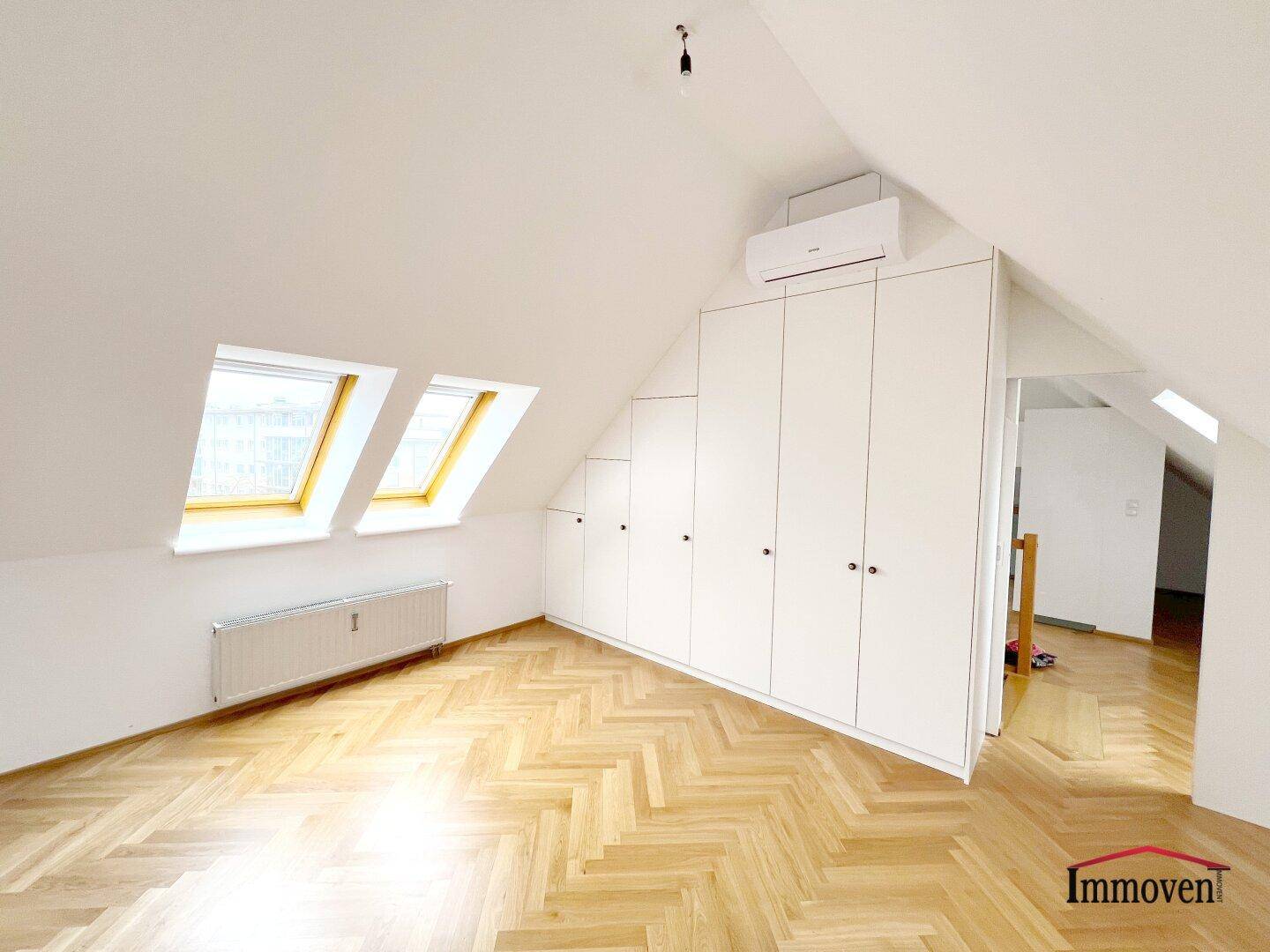 Dachgeschosszimmer mit Parkettboden, Einbauschränken, Dachfenstern und Klimaanlage.