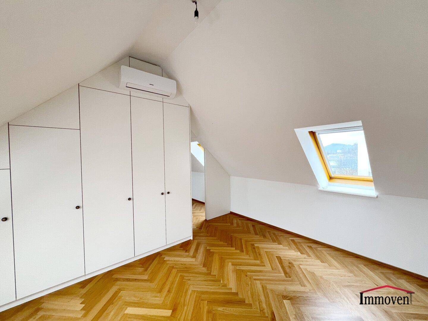 Geräumiges Dachgeschosszimmer mit Parkettboden, Einbauschränken und einem Dachfenster.