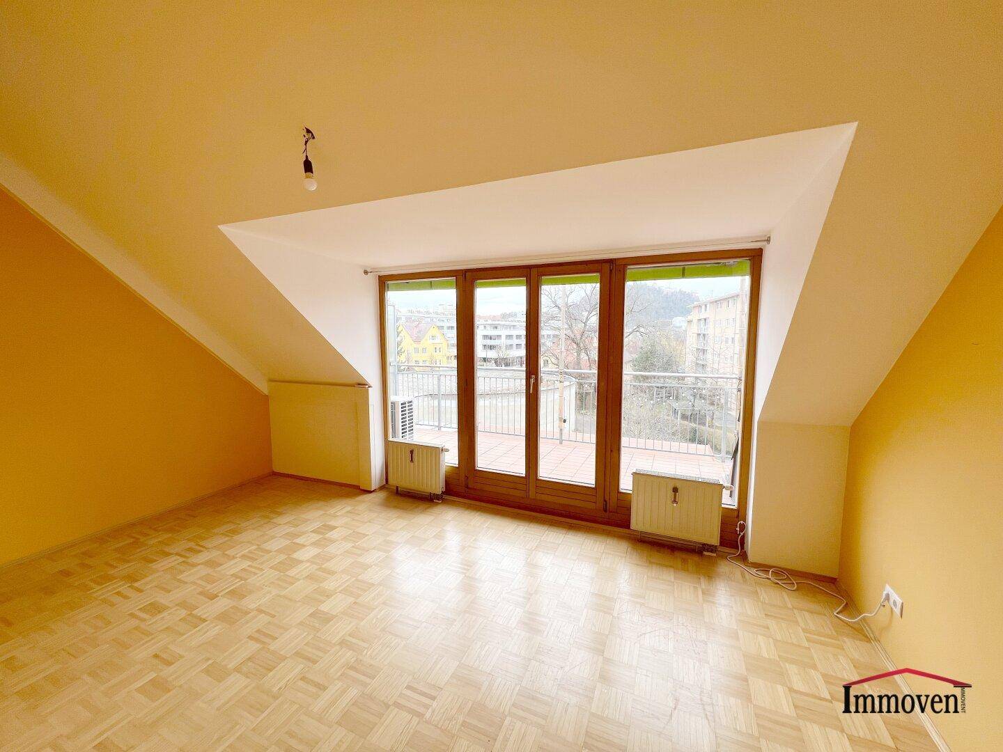 Helles Zimmer im Dachgeschoss mit Parkettboden, schrägen Wänden und Zugang zu einer Terrasse.