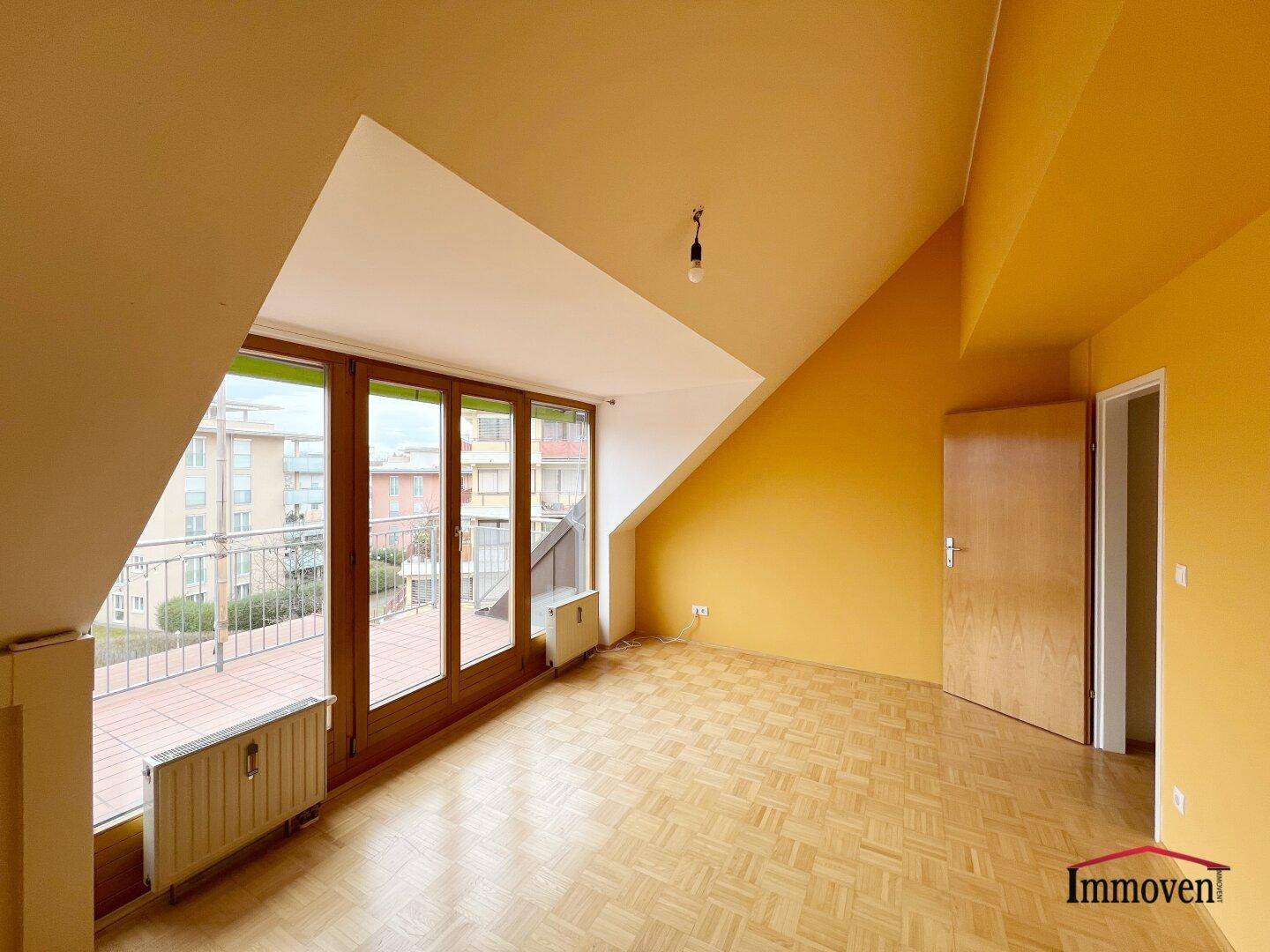 Geräumiges Dachgeschosszimmer mit Parkettboden, schrägen Wänden und Zugang zu einem Außenbereich.