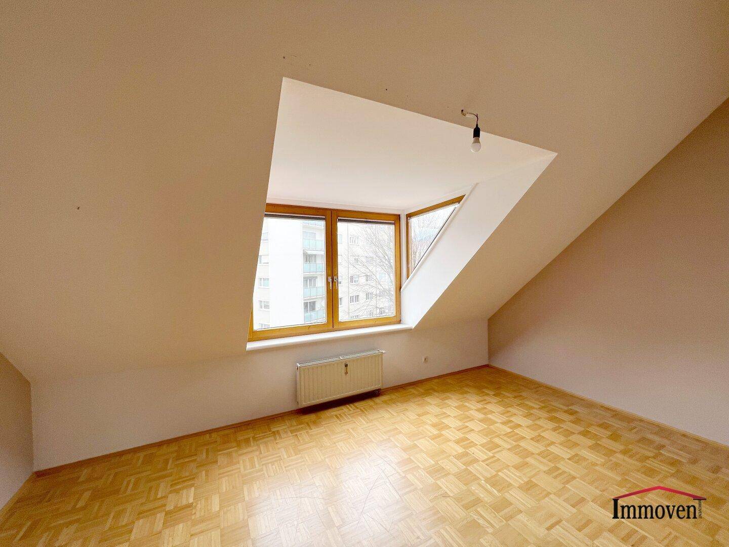 Dachgeschosszimmer mit Parkettboden, schrägen Wänden und einem großen Dachfenster für viel Licht.