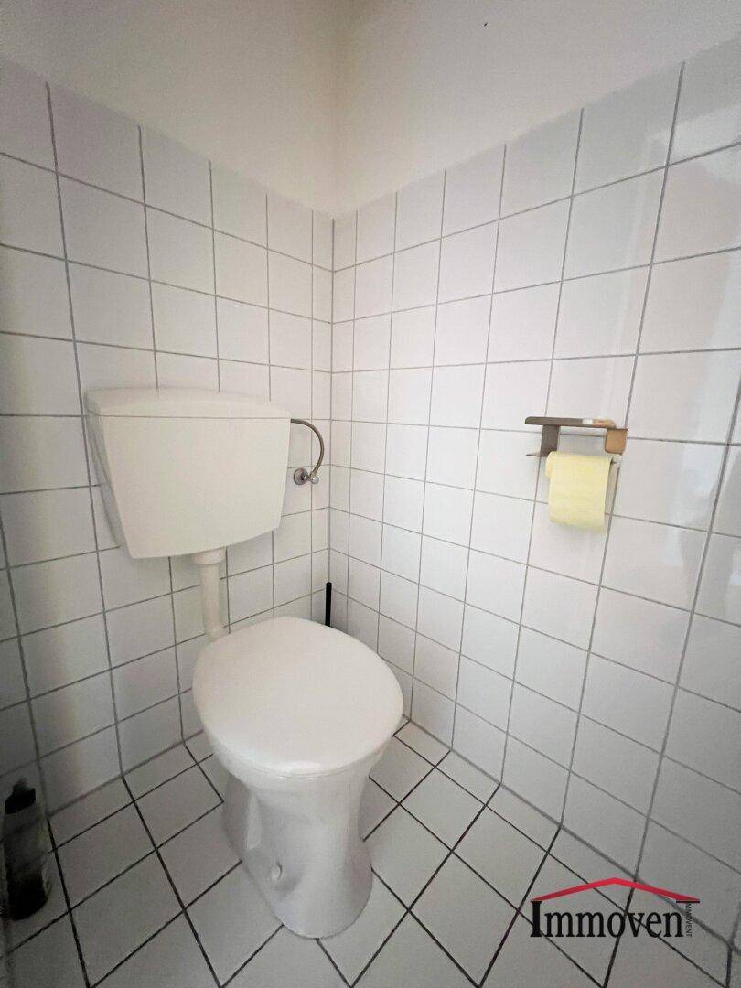 Kleines, vollständig gefliestes WC mit Toilette und weißer Keramik.