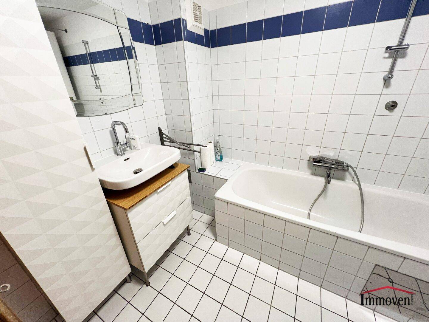 Gefliestes Badezimmer mit Badewanne, Waschbecken und einem Spiegelschrank in weiß-blauer Farbgebung.