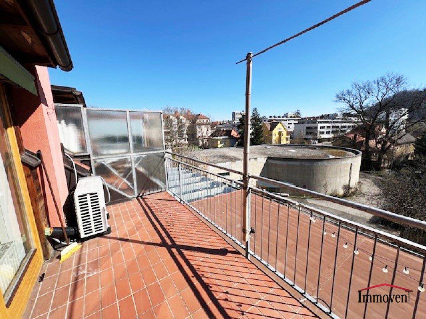 Sonniger Außenbereich mit Fliesenboden, Geländer und Blick auf die umliegenden Gebäude.
