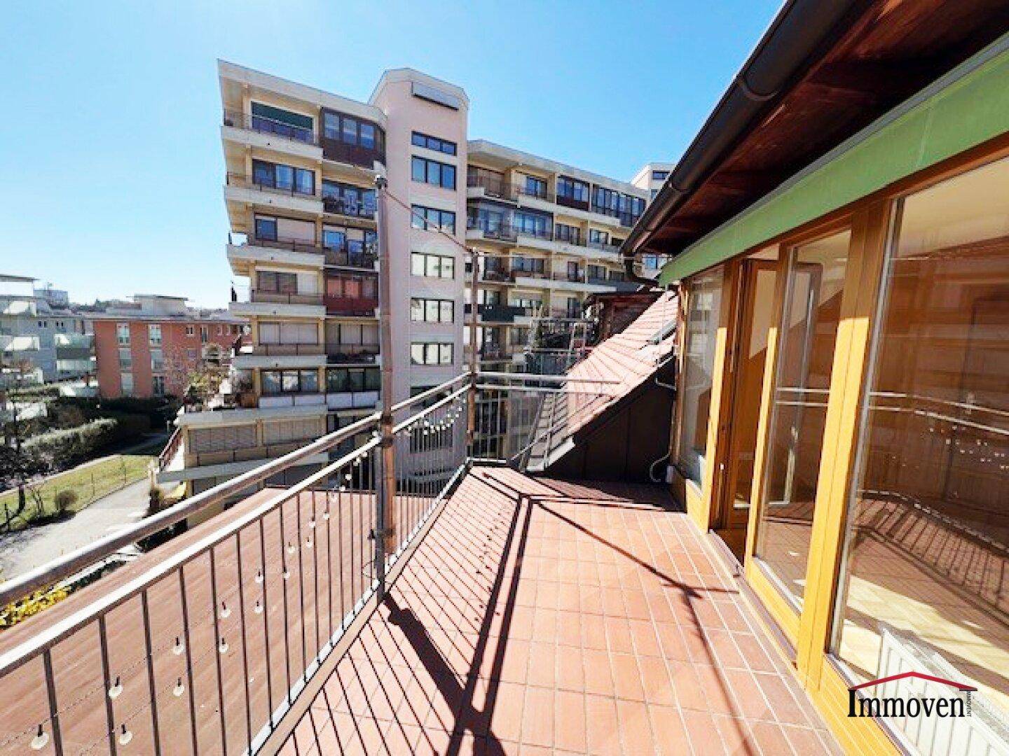 Weitläufige Dachterrasse mit Fliesenboden und Panoramablick auf die Stadt und ein modernes Gebäude.