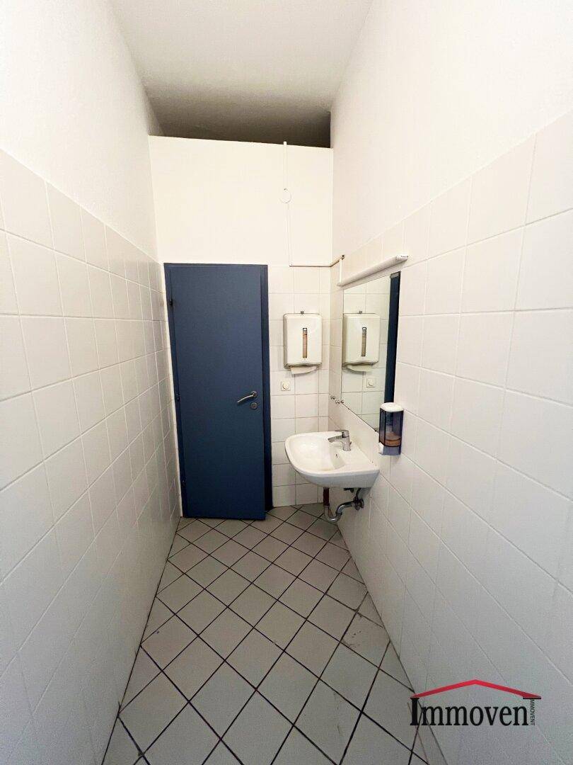 Kleine Gästetoilette mit Waschbecken, Spiegel und weißen Fliesen an den Wänden.