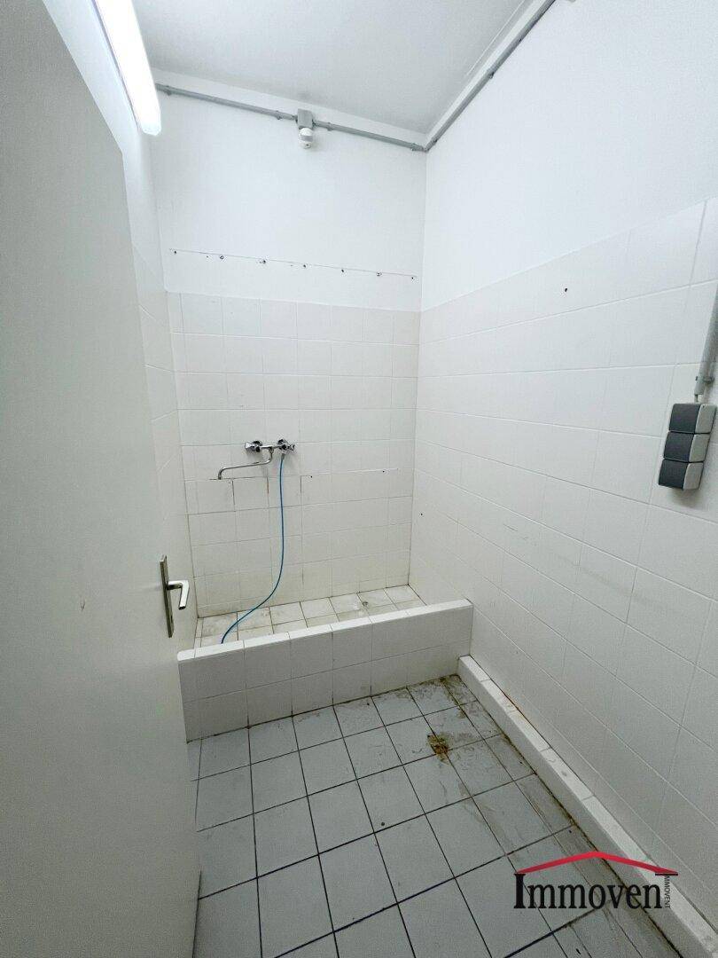 Einfacher Duschraum mit weißen Fliesen an Wänden und Boden, sowie einem Wasseranschluss.