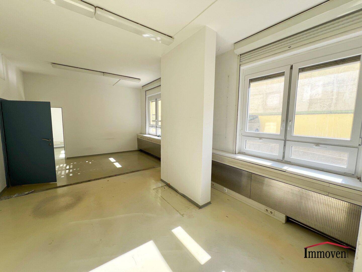 Büroraum mit Säule, großen Fenstern und Heizkörpern unter den Fensterbänken, gut beleuchtet.