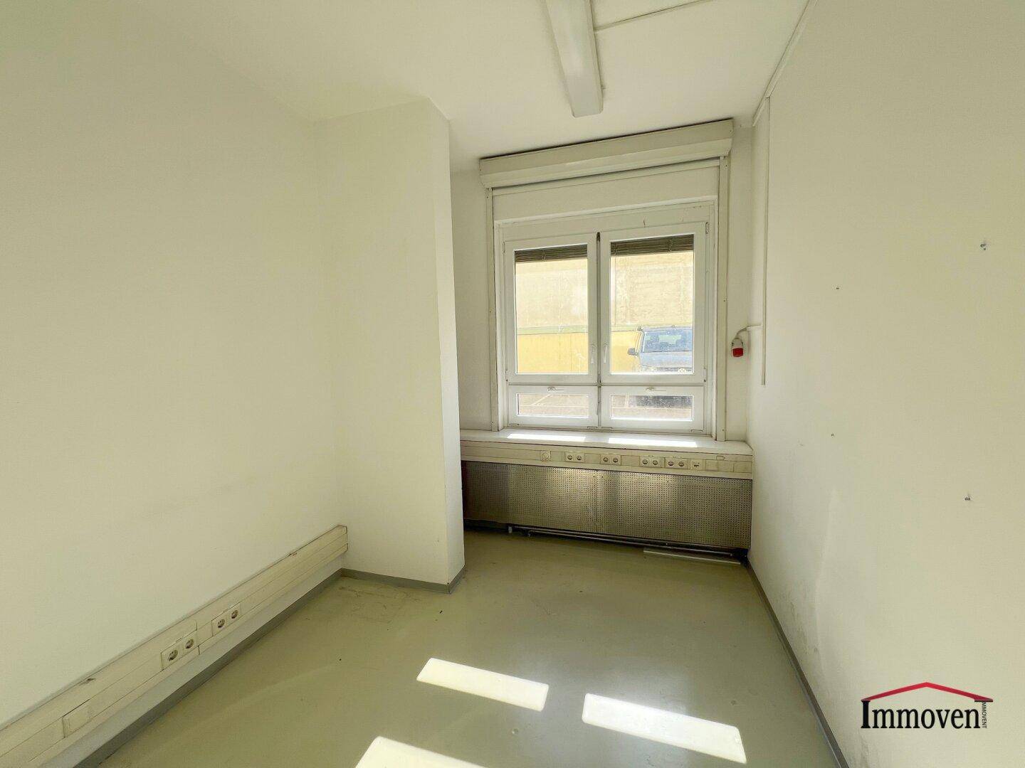 Kleinerer Büroraum mit einem großen Fenster, Jalousien und viel natürlichem Lichteinfall.