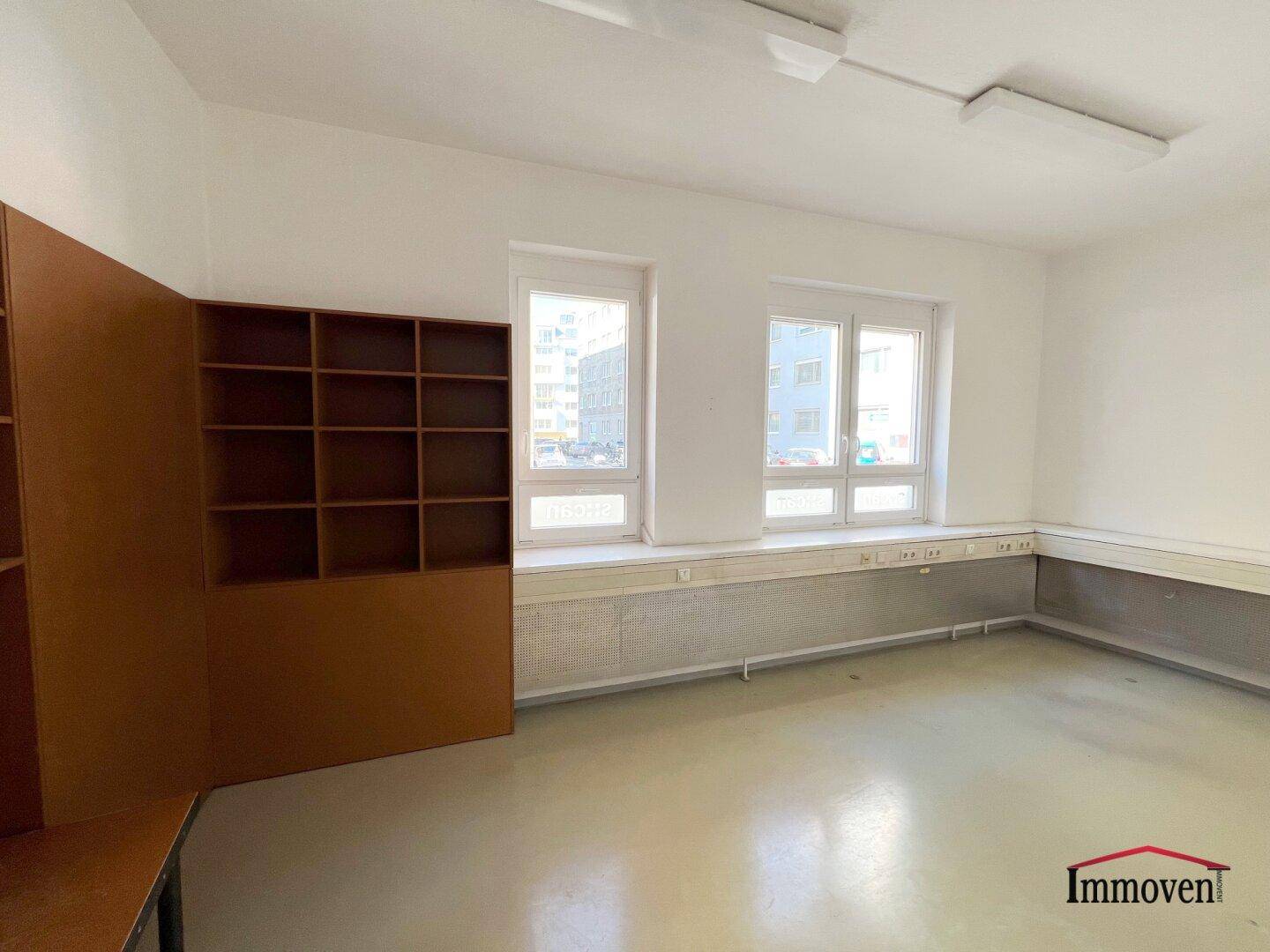 Büroraum mit einem großen Regal und zwei Fenstern, die viel natürliches Licht spenden.