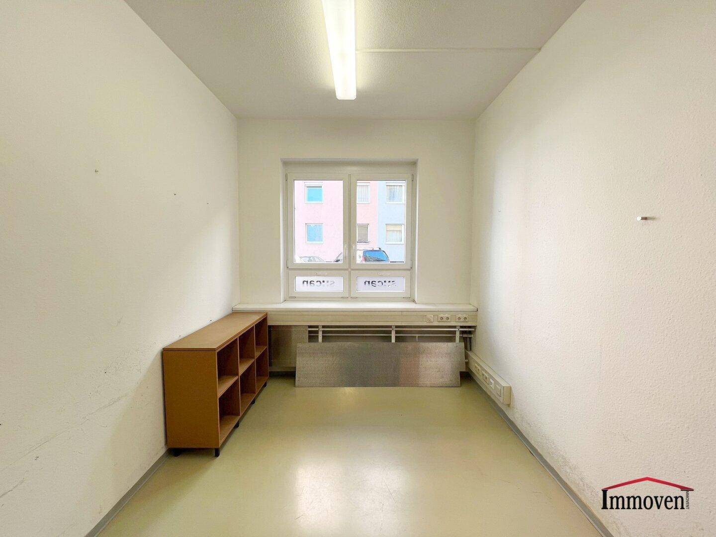 Kleiner Büroraum mit einem Fenster, einem Regal und viel Tageslicht.