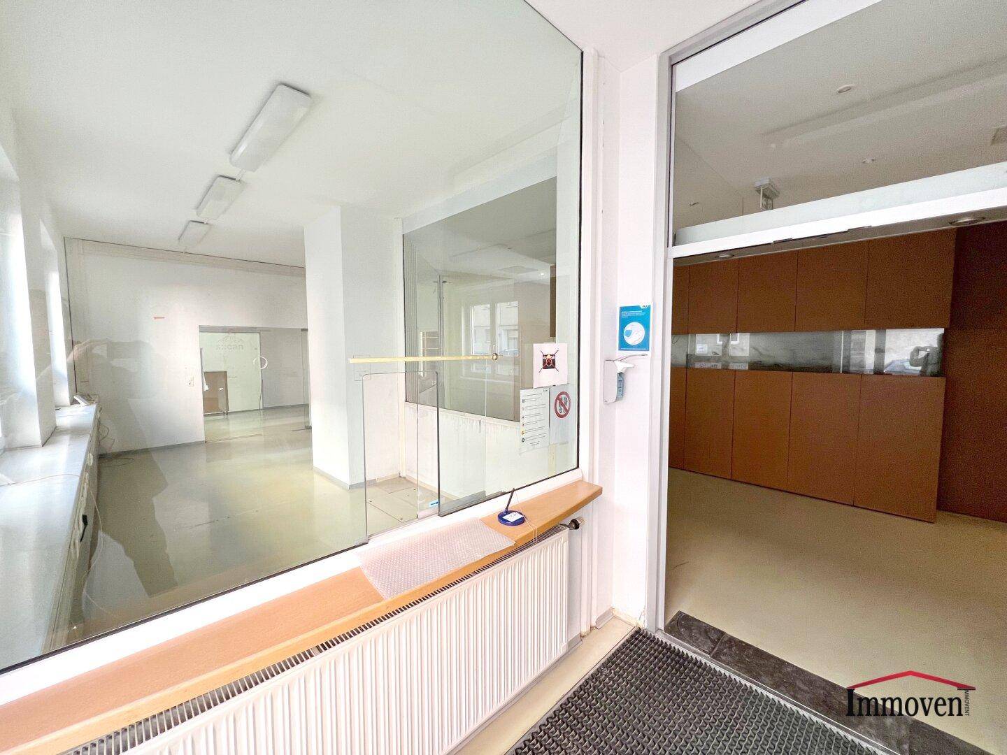 Empfangsbereich mit Glasabtrennung und Blick auf eine lange Fensterfront mit Heizkörpern.