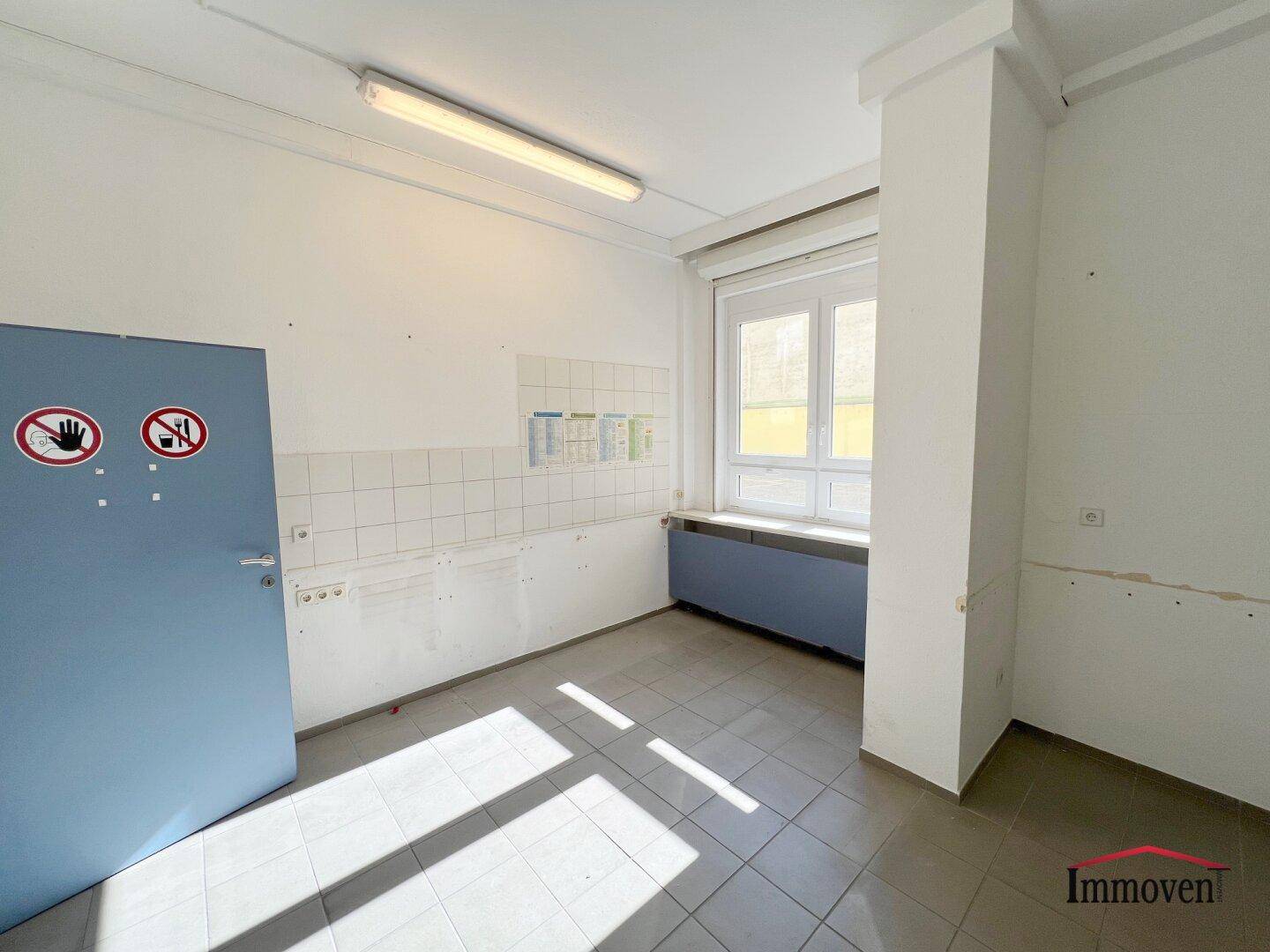 Funktionaler Raum mit Fliesenboden, Fenster und einer blauen Tür mit Warnhinweisen.