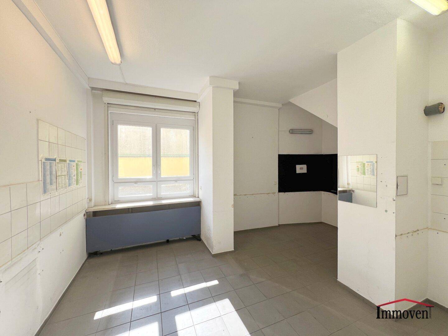Einfacher Raum mit Fliesenboden, Fenster und vorbereiteten Anschlüssen für eine Küche.