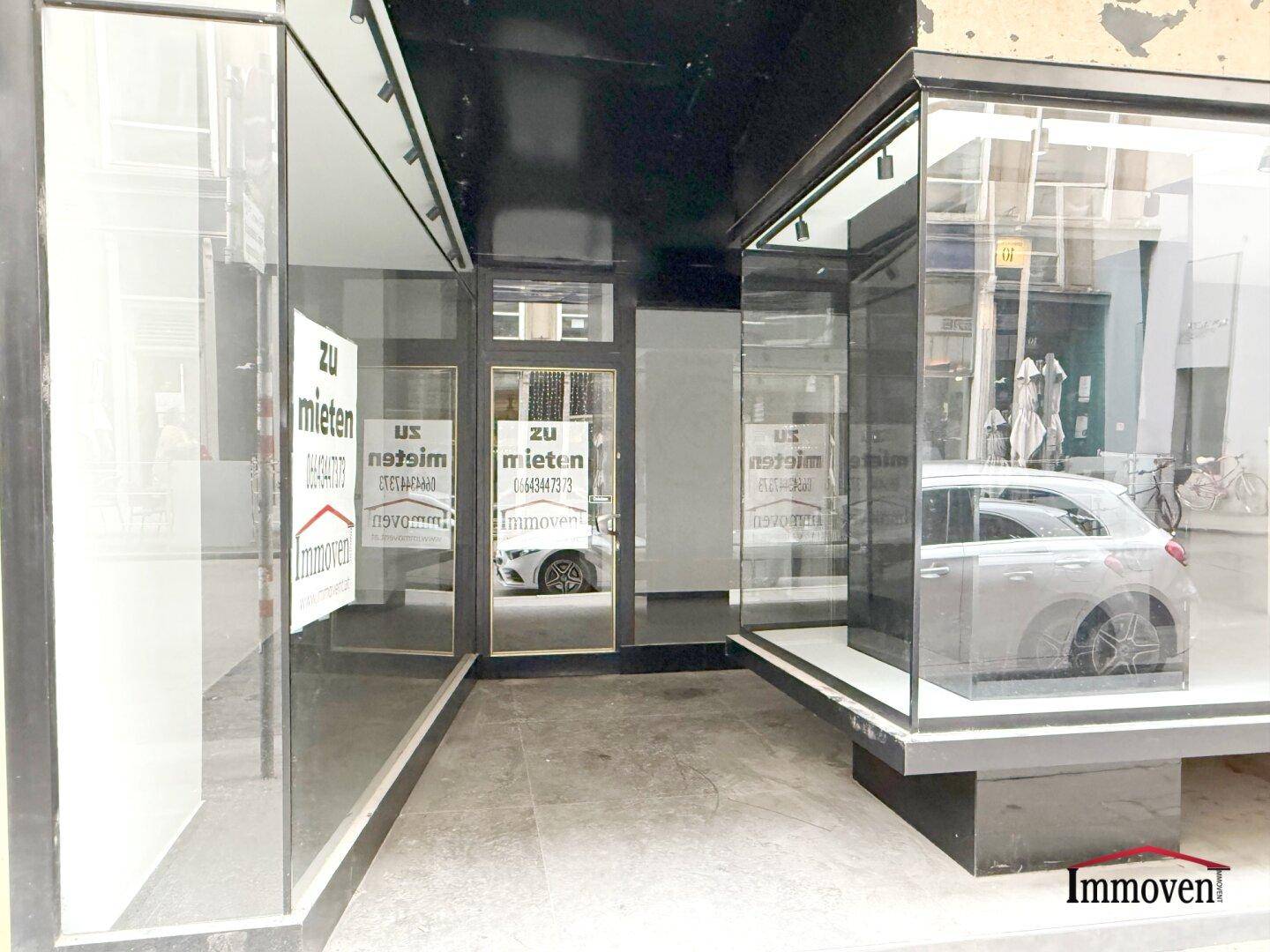 Nahaufnahme des Eingangs und der Schaufenster eines Ladenlokals mit reflektierenden Glasflächen.