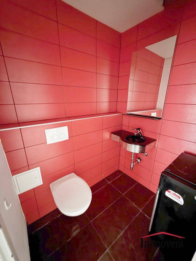 Kleine Toilette mit leuchtend roten Fliesen an den Wänden und einem modernen schwarzen Waschbecken.