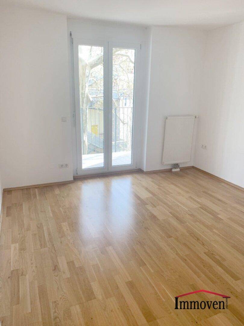 Heller Raum mit Parkettboden und großem Fenster, das Zugang zu einem französischen Balkon bietet.