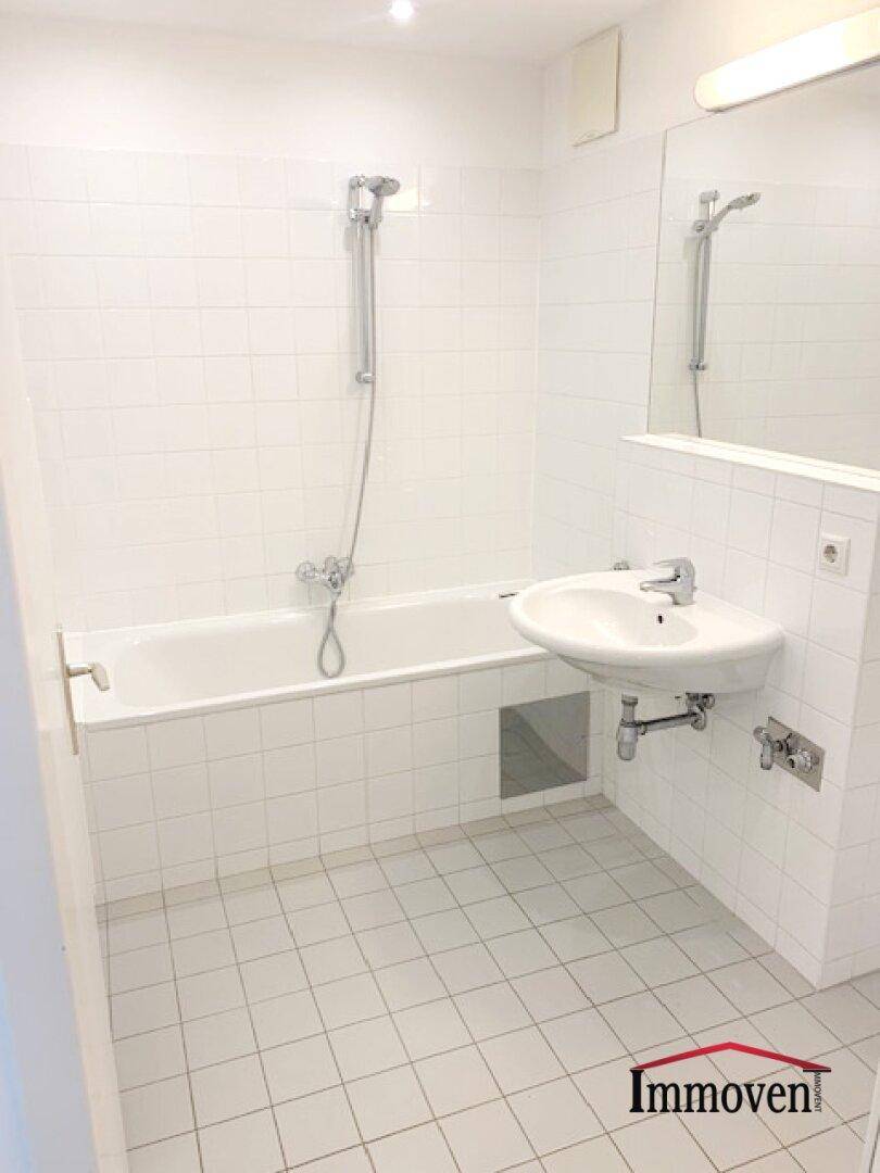Helles Badezimmer mit weißen Fliesen, Badewanne mit Duschfunktion und einem Waschbecken.