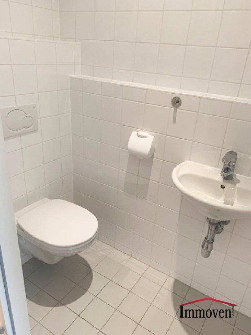Separates WC mit wandhängender Toilette, kleinem Waschbecken und weißen Fliesen.