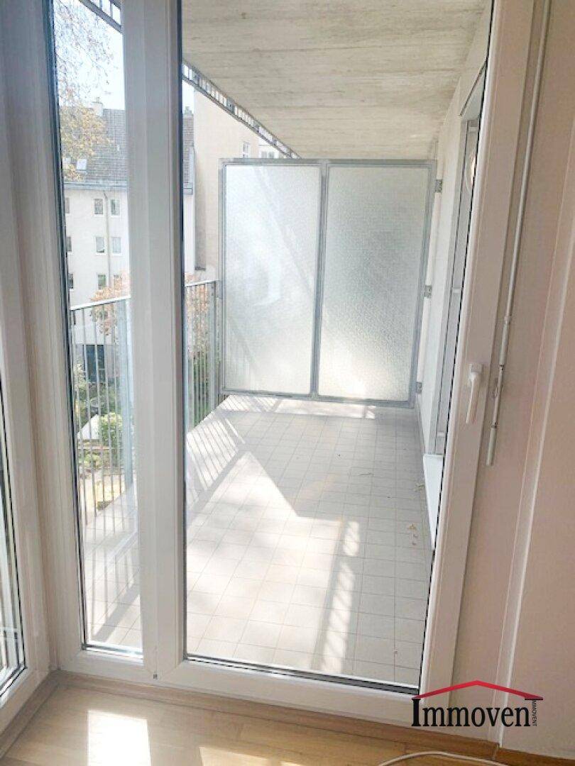 Geräumiger Balkon mit Fliesenboden und Blick auf die umliegenden Gebäude und Grünflächen.